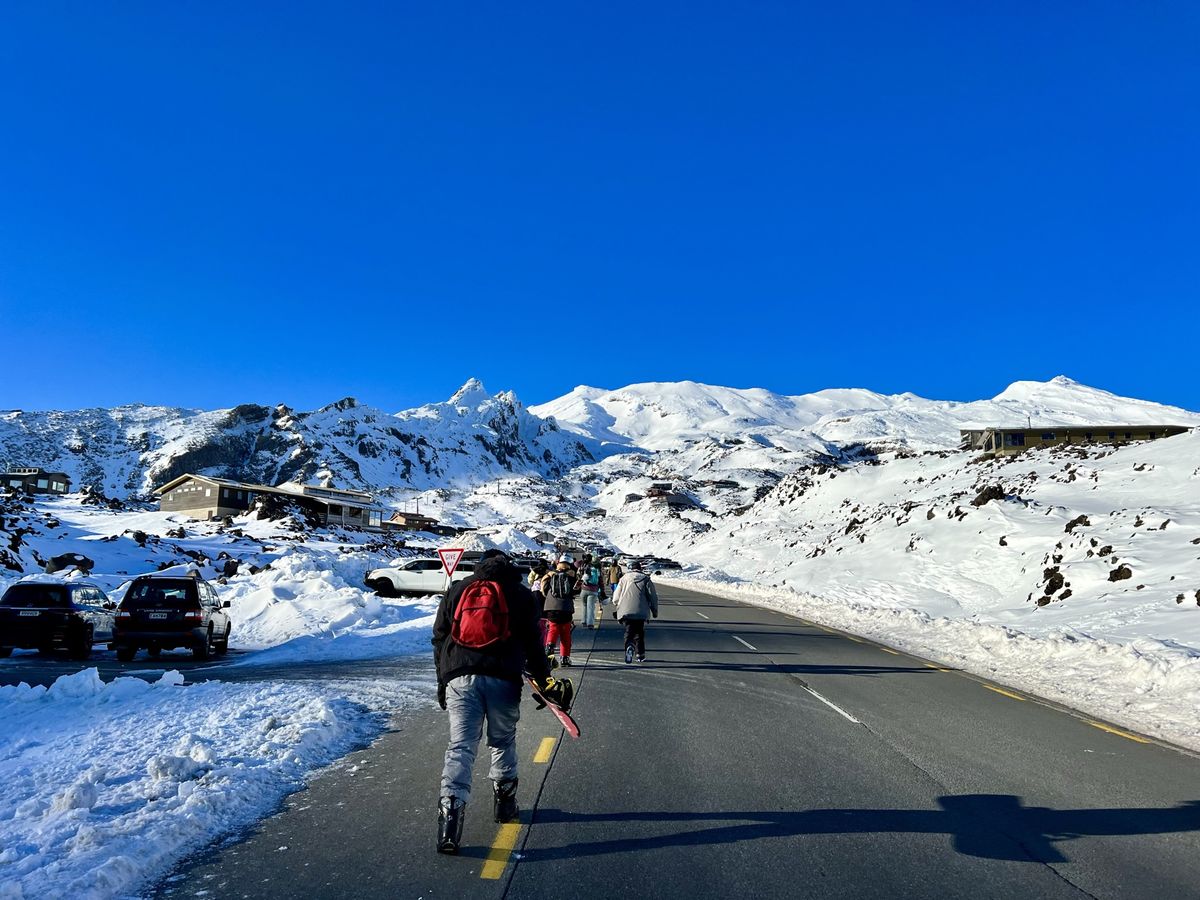 a group of people walking up a snow covered road towards the Whakapapa ski field.