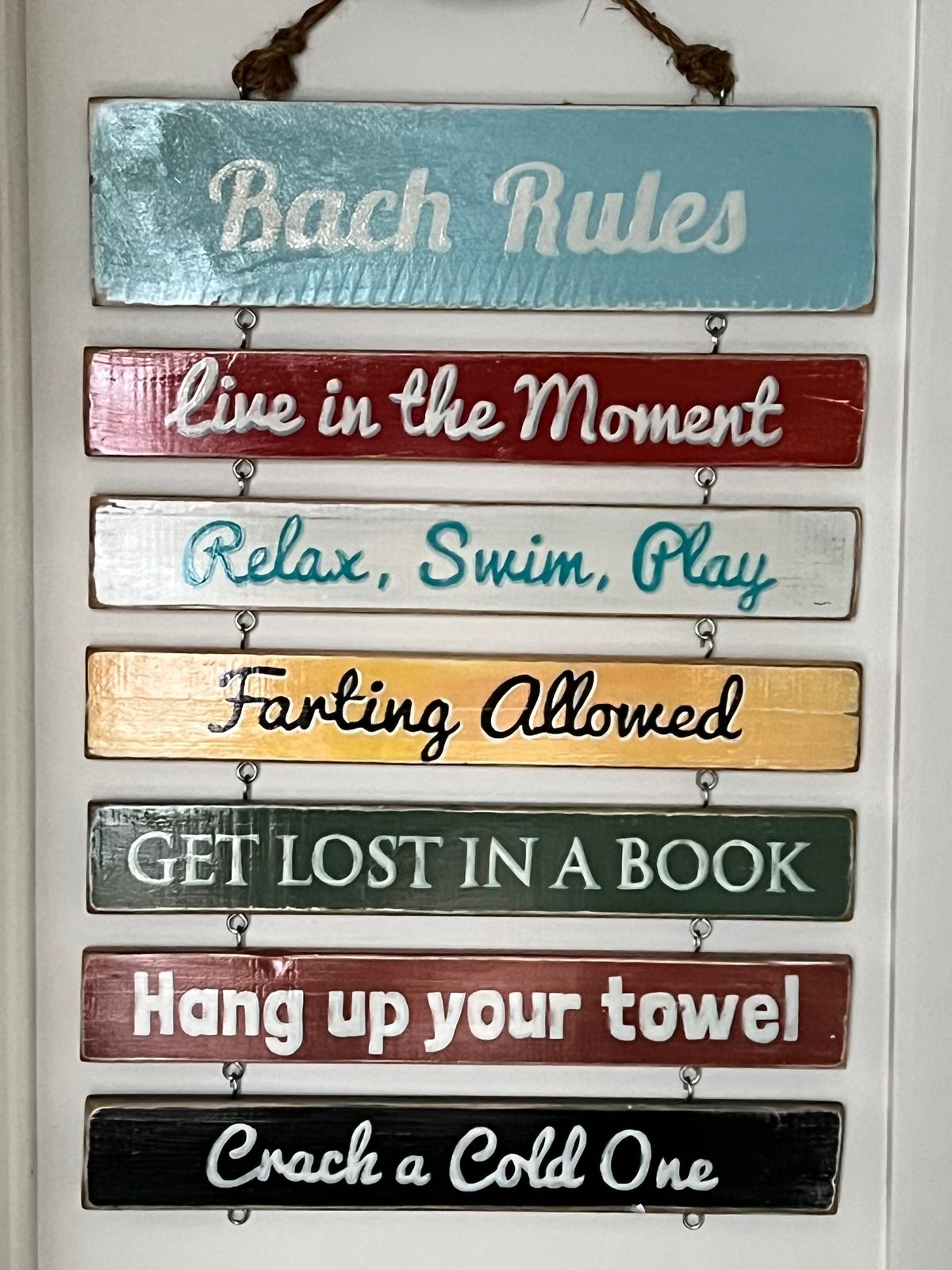 Hanging wooden sign displays multiple colorful planks with phrases 